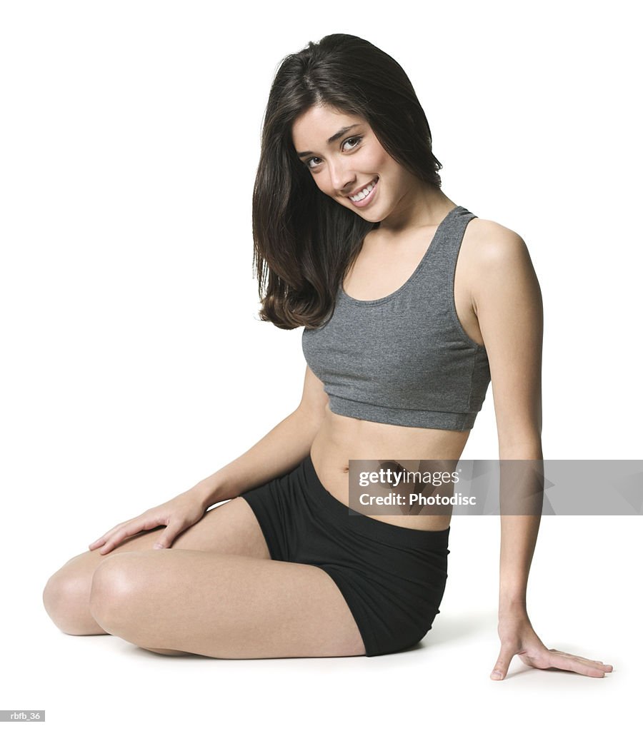 Full body shot of a young adult woman in a black and grey exercise outfit as she sits and smiles