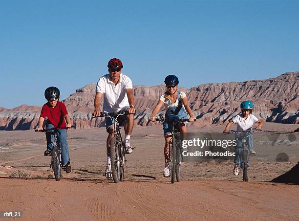 young family of four ride on their bikes across desert wearing helmets - across stock pictures, royalty-free photos & images