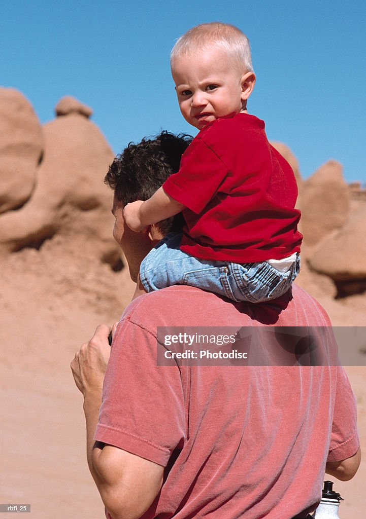 A father gives his toddler a piggy-back-ride through red rock desert