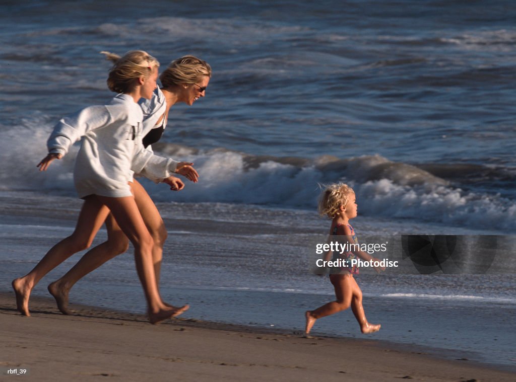 A mother and teenage daughter run after a toddler on the beach