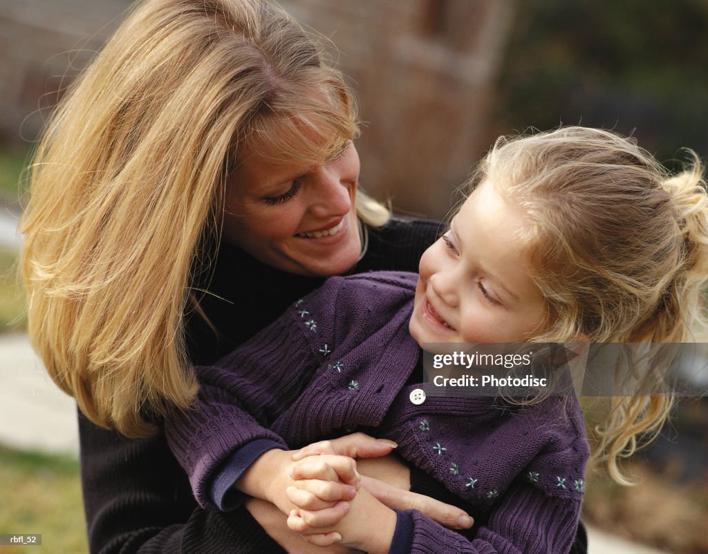 A blone happy mother hold daughter and makes her laugh