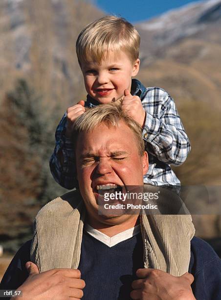 a little boy on his dad's shoulders pulls his hair and smiles - hair pulling stock pictures, royalty-free photos & images
