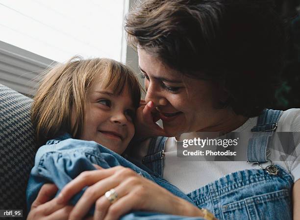 a little girl grabs her mother's nose as she cuddles her - pinching nose stockfoto's en -beelden