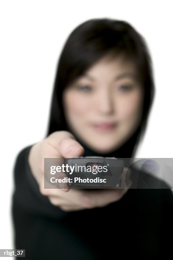 Medium shot of a young adult woman as she points a remote control at the camera Medium shot of a young adult woman as she points a remote control at the camera