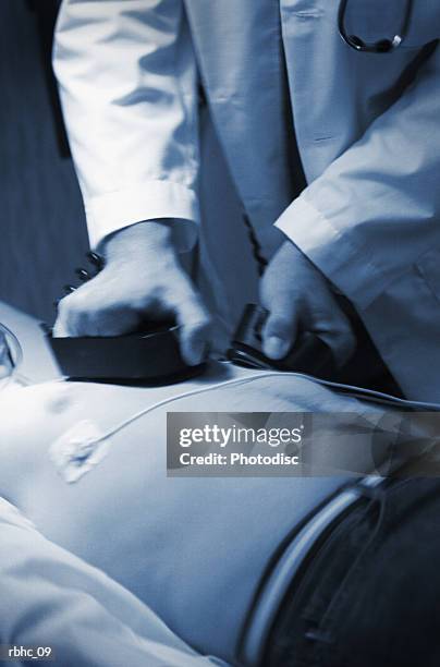 a doctor tries to resuscitate a male caucasain patient using crash cart paddles - resuscitate stock pictures, royalty-free photos & images