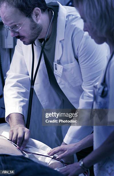 a male caucasian doctor and a nurse use a stethoscope to check the heartbeat of a accident victim - check up ストックフォトと画像