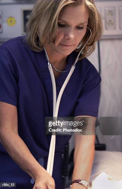 a blonde caucasian nurse in scrubs works on a patient in the er - er stock-fotos und bilder