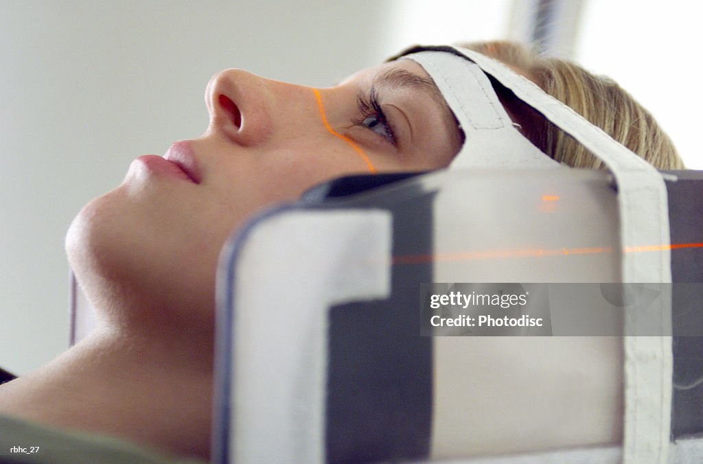 Close up of a blonde caucasian female patient as her head is strapped into a cat scan machine