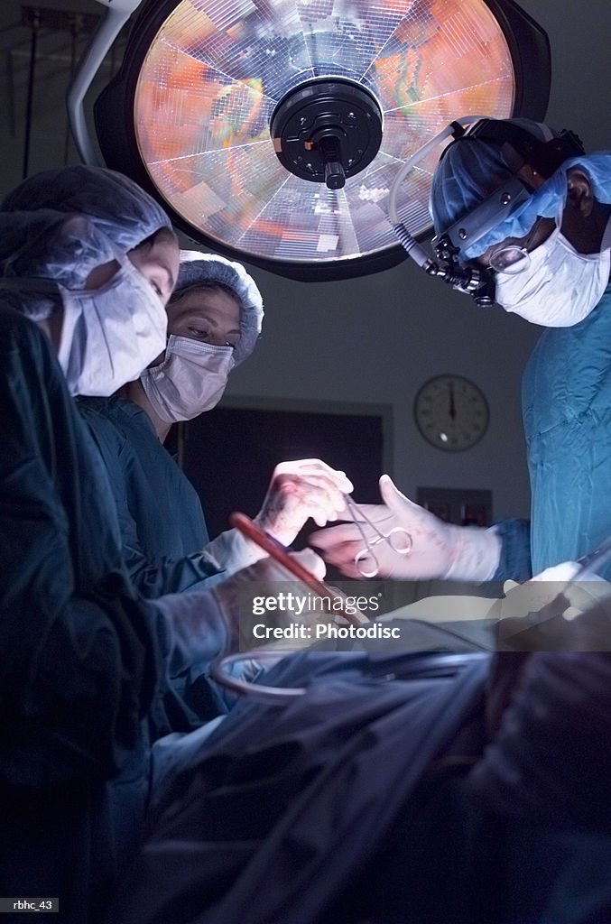 A group of doctors perform an operation as on nurse hands the surgeon a tool