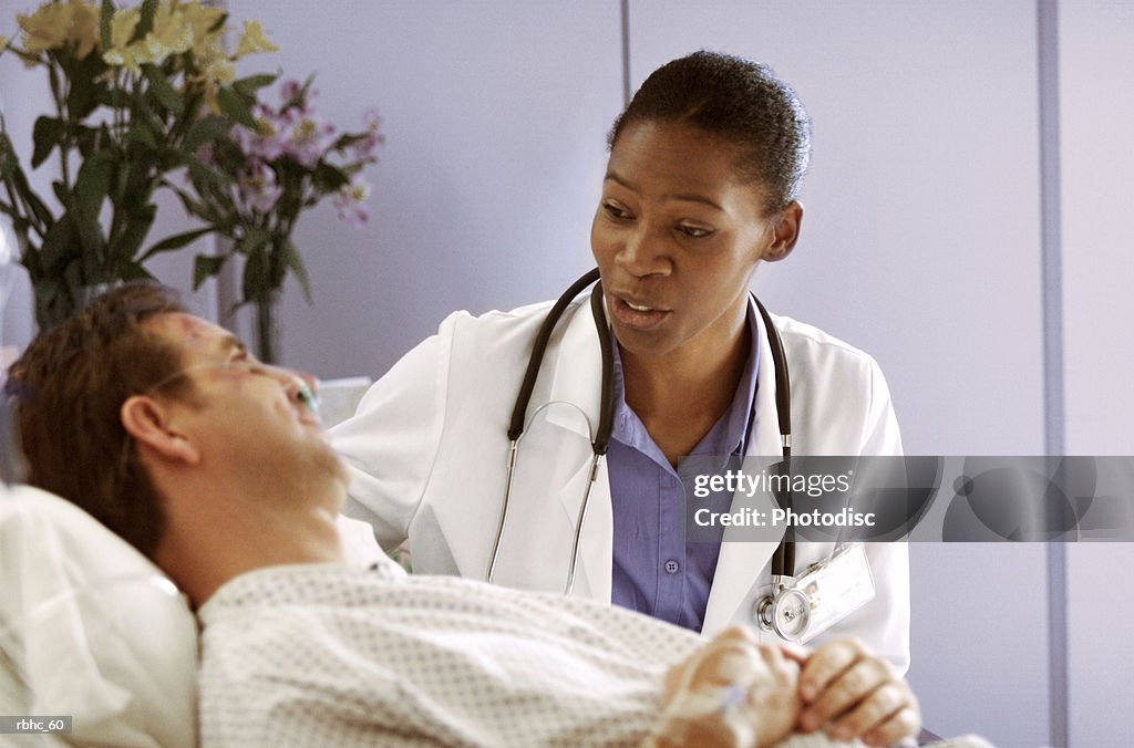 An african american doctor consults with a male caucasian patient as he lies in a hospital bed
