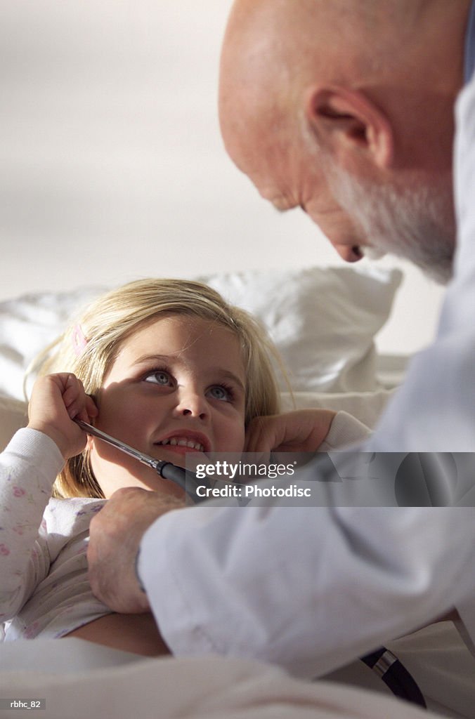 A little caucasain blonde girl plays with an elderly doctors stethoscope as he visits her in a hospital room