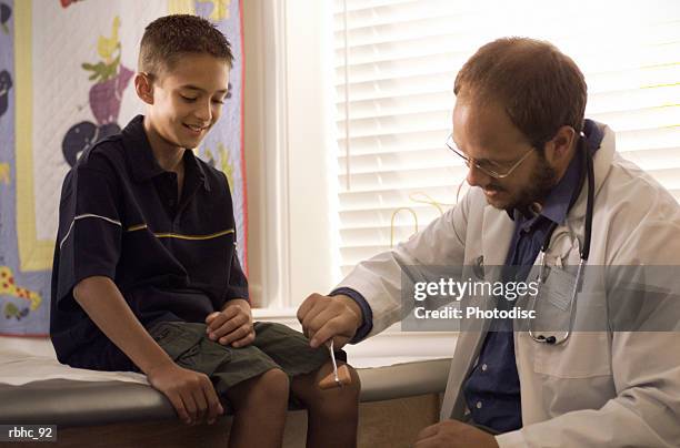 a caucasian male pediatricain checks the relexes on a young boy in his examination room - reflex hammer stock pictures, royalty-free photos & images