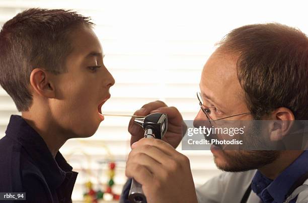 caucasian male pediatrician with beard examines the throat of a young boy patient during a check up - check up ストックフォトと画像