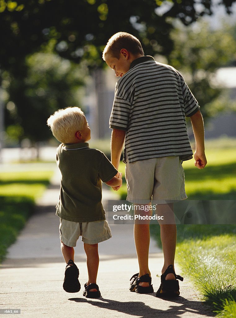 Two caucasian brother go for a walk down a sidewalk