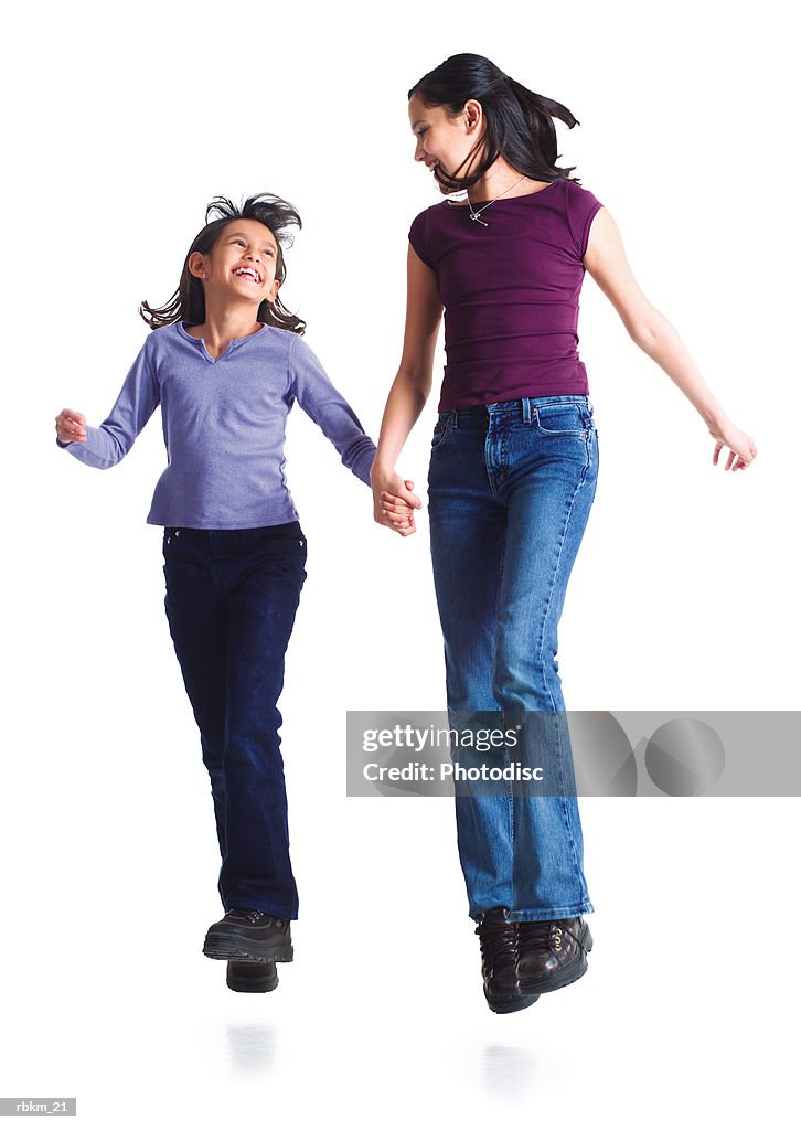 Two young sisters jump into the air laughing while holding hands