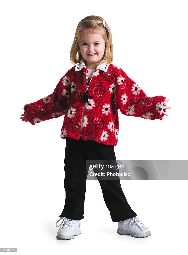 A little blonde girl in a red flower patterned sweater smiles and holds her arms open
