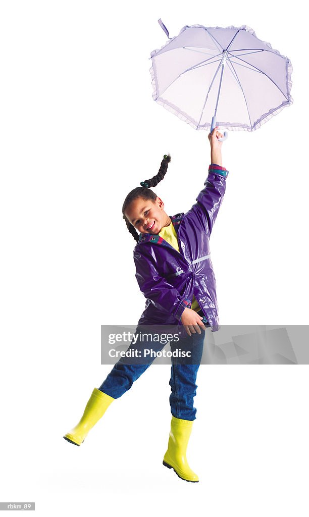 A cute little african american girl in a rain jacket jumps into the air with her umbrella
