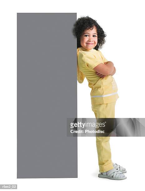 an ethnic looking female child in a yellow outfit folds her arms and leans against a blank sign - kid arms crossed stock pictures, royalty-free photos & images