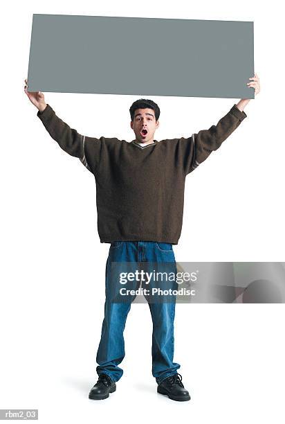 a young ethnic looking man in jeans and a brown sweater holds a large sign above his head - soul patch stock pictures, royalty-free photos & images