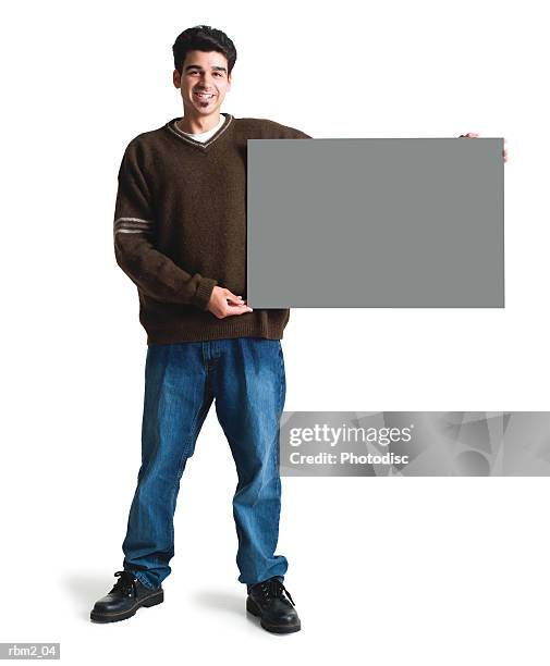 a young ethnic looking man in jeans and a brown sweater holds a large blank sing to his side - pelo facial fotografías e imágenes de stock