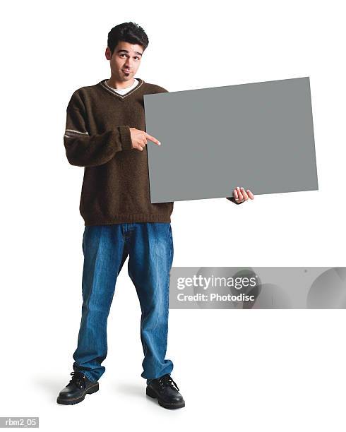 a young ethnic looking man in jeans and a brown sweater points to a large sign by his side - ソウルパッチ ストックフォトと画像