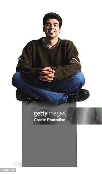a young looking man in jeans and a brown sweater sits atop a blank sign with his legs folded - soul patch stock pictures, royalty-free photos & images