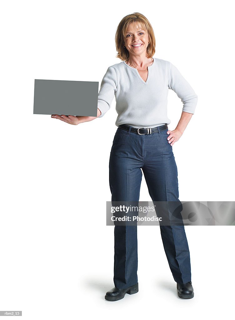 A caucasian woman in blue pants and a grey blouse holds a  sign in the palm of her hand