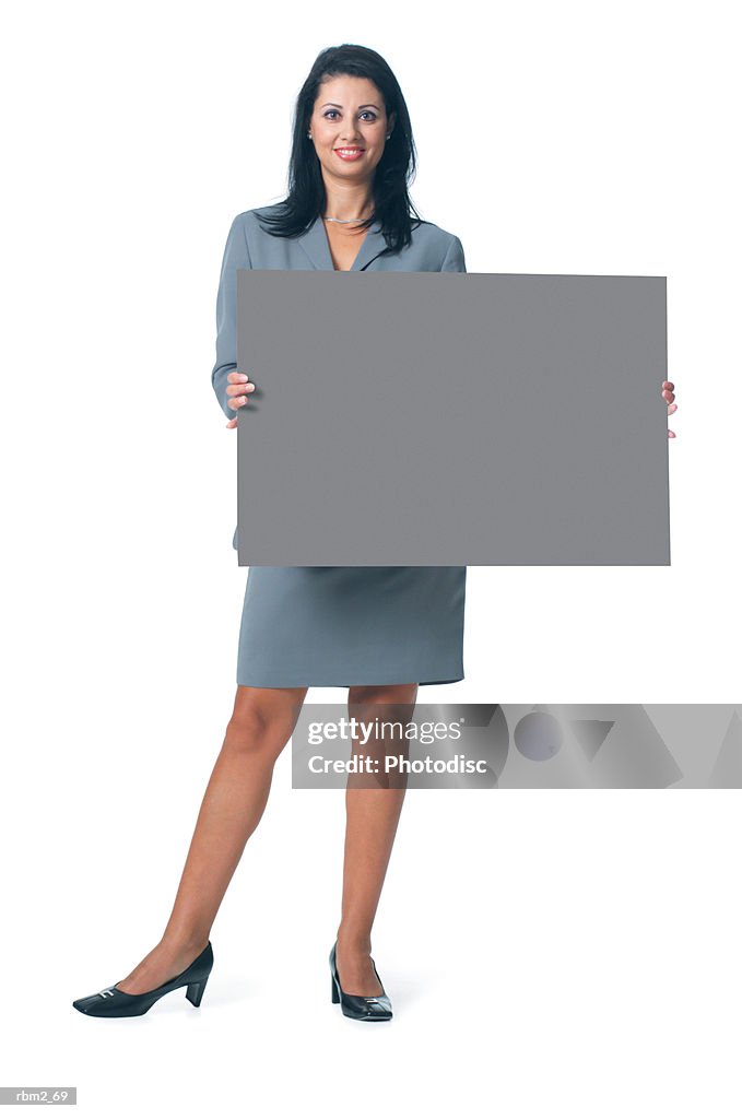 An adult ethnic female in a grey business outfit holds a blank sign out in front of herself