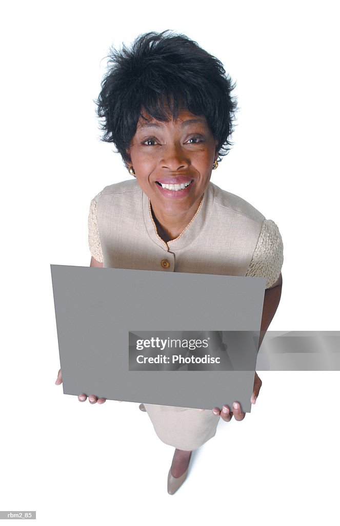 An adult african american woman in a tan dress holds a sign and smiles up at the camera
