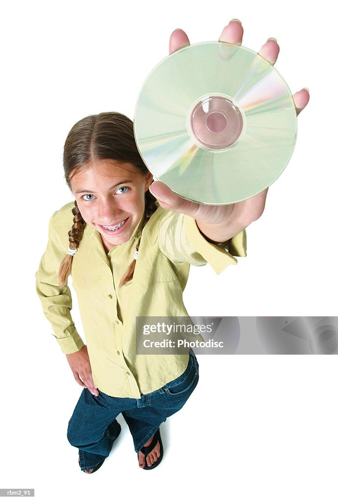 A teenage caucasian girl in jeans and a green shirt holds up a cd as she smiles up into the camera