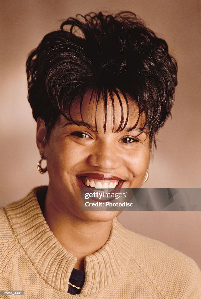 A beautiful happy african american woman in a tan sweater laughs and smiles for the camera