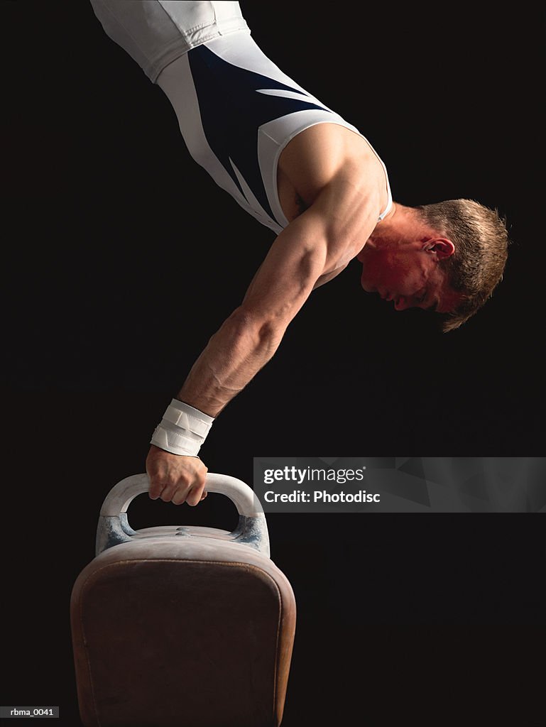 A strong male gymnast does a handstand on the pommel horse