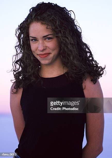 a vertical image of a young woman with long curly hair who gives a shy smile - curly stock pictures, royalty-free photos & images