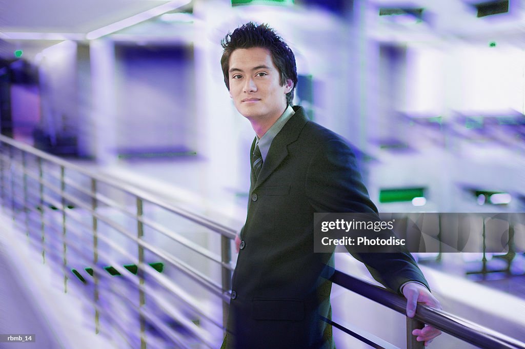 Portrait of a young asian business man in a dark suit as he laens against a railing