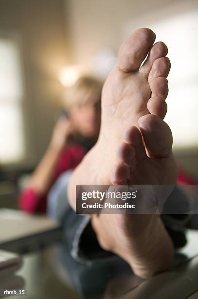 a blonde woman leans back in her chair while on the phone and puts her bare feet on the desk - bare back stock-fotos und bilder