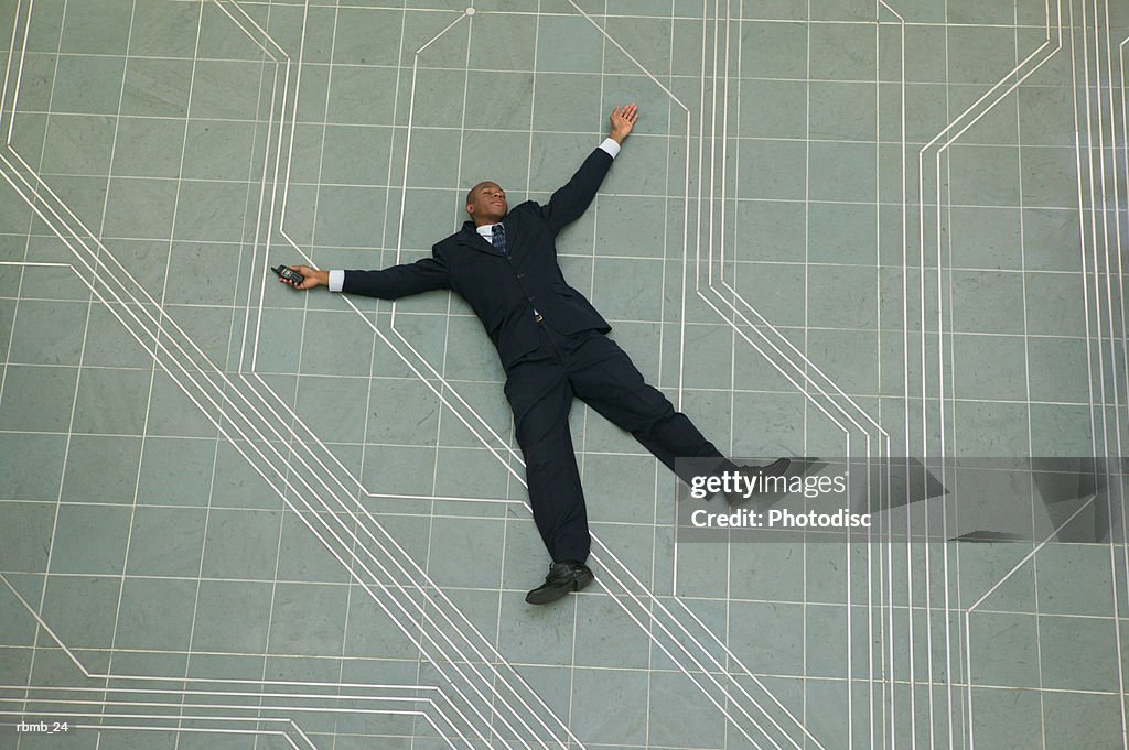 Conceptual shot of an african american business man as he lays flat on the ground holding his phone