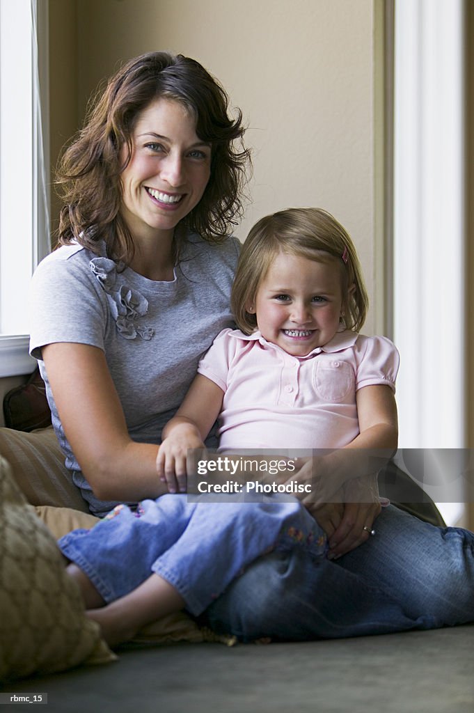 Lifestyle portrait of a mother as she sits on a couch and holds her young daughter