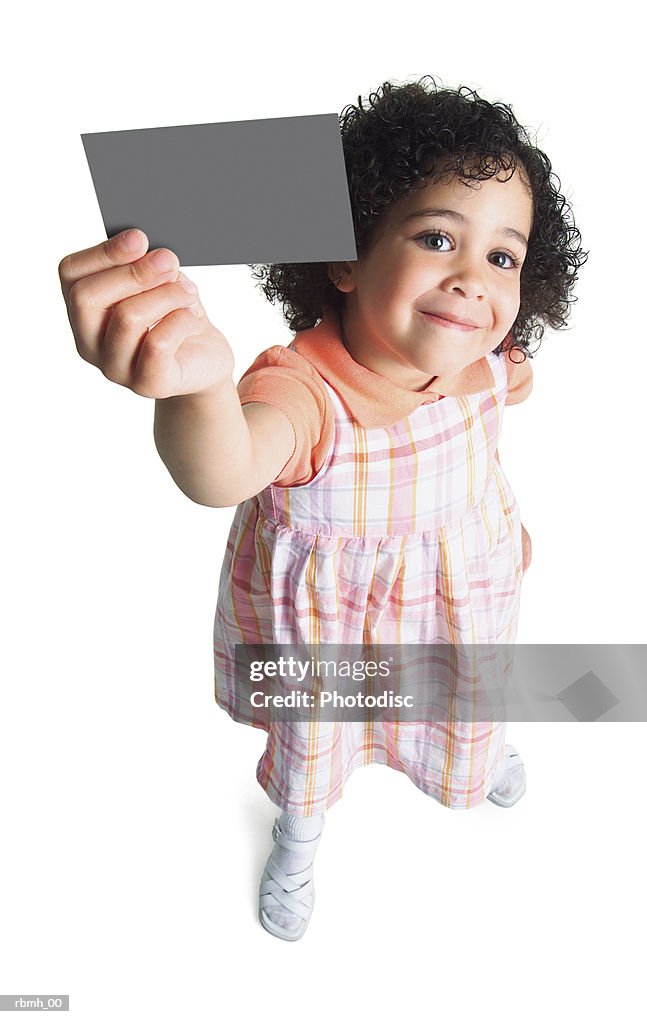 A young ethnic girl in a pastel dress holds a blank sign up to the side of her head and smiles