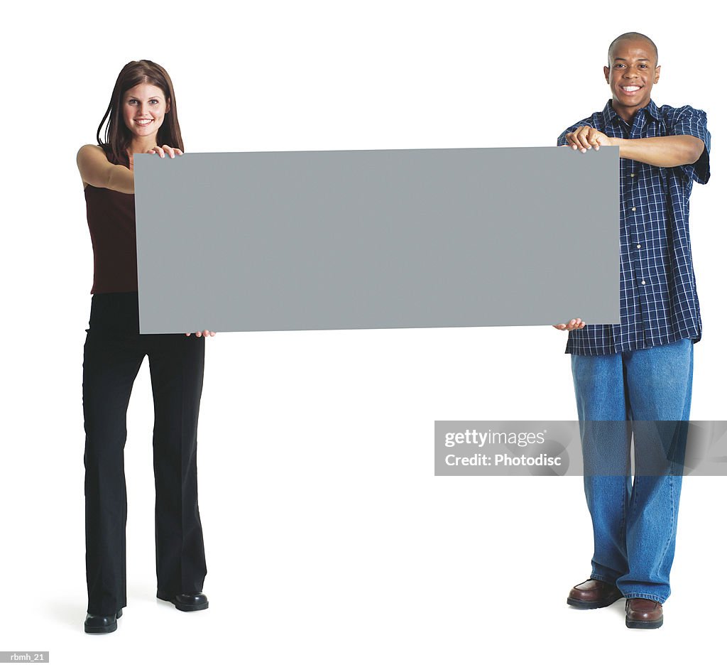 A young attractive caucasian woman and a young african american man hold up a large sign together and smile