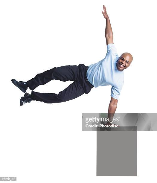 a young bald african american man wearing dark slacks and a light blue shirt jumps up to one side as he balances one hand on a blank sign and extends his other arm above him - bald stock-fotos und bilder