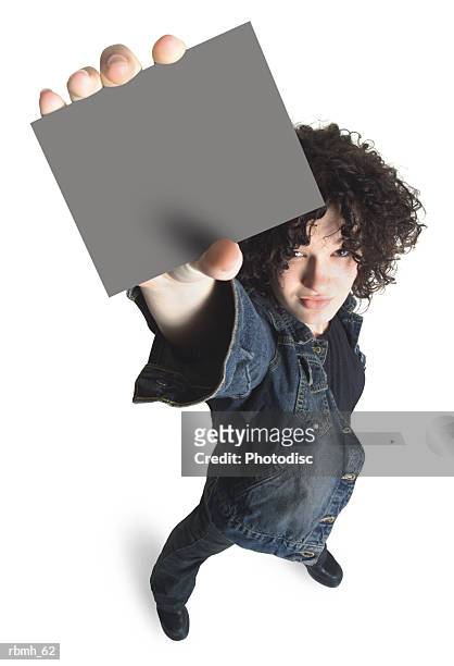 a caucasian girl with brown curly hair wearing jeans and a jean jacket holds a blank sign above her head with one hand as she looks up at the camera - curly stock pictures, royalty-free photos & images