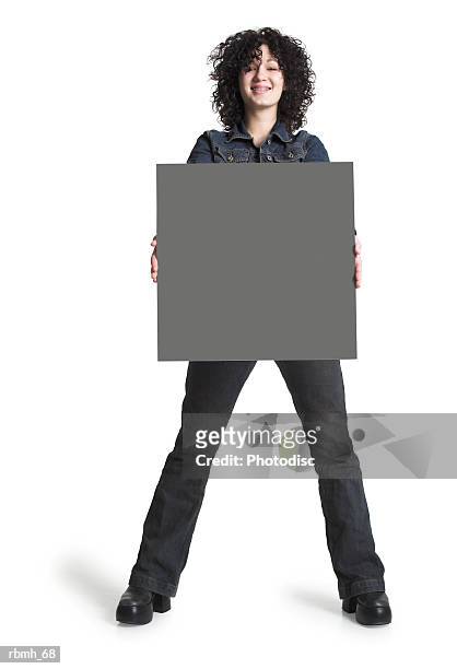 a caucasian girl with brown curly hair wearing jeans a black shirt and a jean jacket holds a blank sign out in front of her with both hands as she smiles and stands with her feet hip distance apart - curly stock pictures, royalty-free photos & images