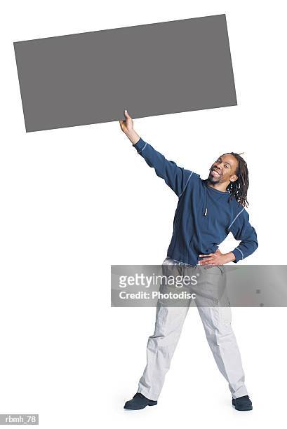 an african american man with dreadlocks wearing kakhi pants and a blue shirt stands with his legs shoulder width apart and he has one hand on his hip and holds a sign up with one hand above his head - hand on head ストックフォトと画像