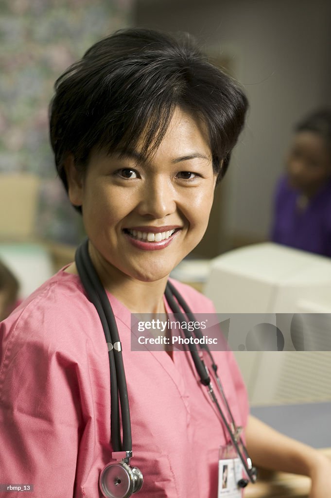 Portrait of an adult female in pink scrubs as she stands by the nurses station and smiles