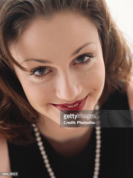 a cute young brunette smiling at the camera wearing a nice black dress and a string of pearls. - string - fotografias e filmes do acervo