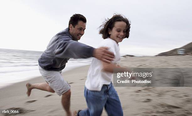 a caucasian father chases his daughter on the beach laughing - tag game fotografías e imágenes de stock