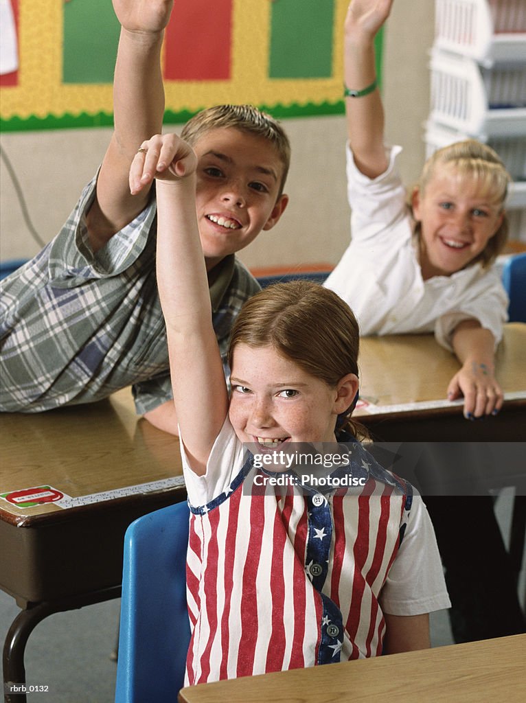 A group of students at their desks enthusiastically raise their hands to answer a question