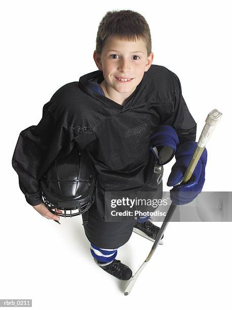 child caucasian male hockey player in black holds stick and helmet and smiles looking up to camera - ice hockey uniform stock pictures, royalty-free photos & images