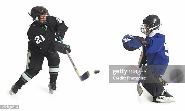 two child caucasian male hockey players from opposing teams confront each other when one shoots the puck as the goalie tries to block - ijshockeytenue stockfoto's en -beelden