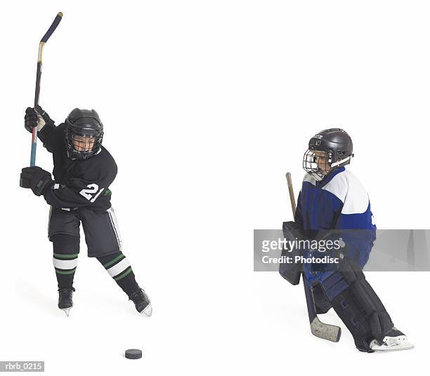 two child caucasian male hockey players on opposing teams face off as one prepares to shoot as the goalie gets ready to block - ijshockeytenue stockfoto's en -beelden